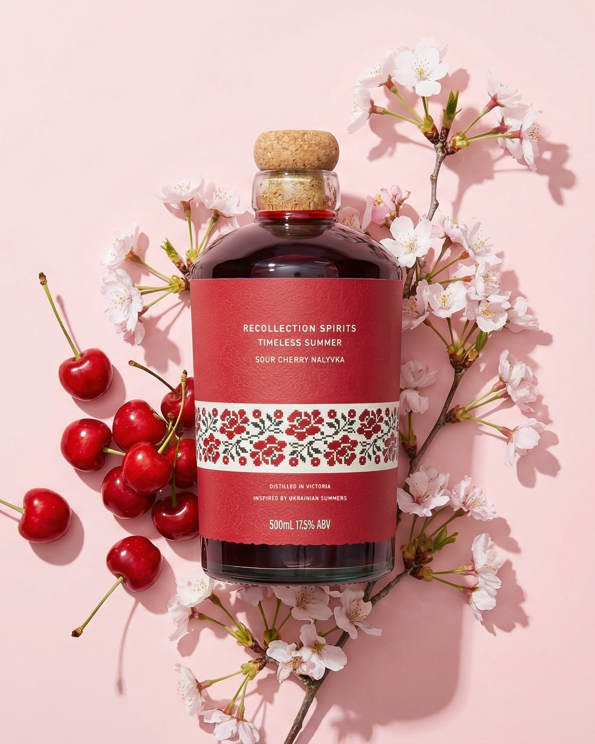 Bottle of cherry-flavored liqueur with cherries and flowers on a pink background