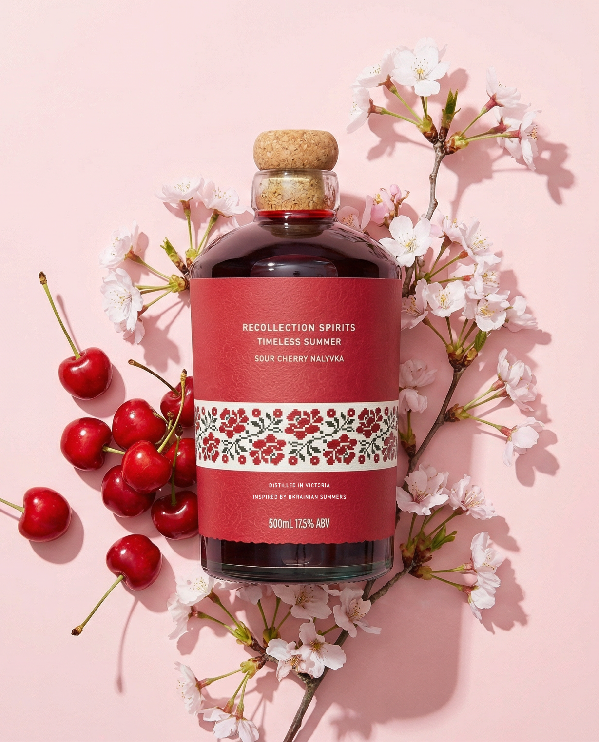 Bottle of cherry-flavored liqueur with cherries and flowers on a pink background