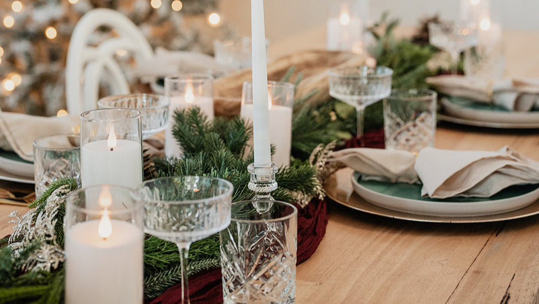 Decorative Christmas table setting with candles and a tree in the background.