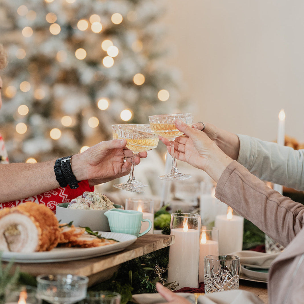 Two people toasting with glasses at a festive dinner table with a Christmas tree in the background.